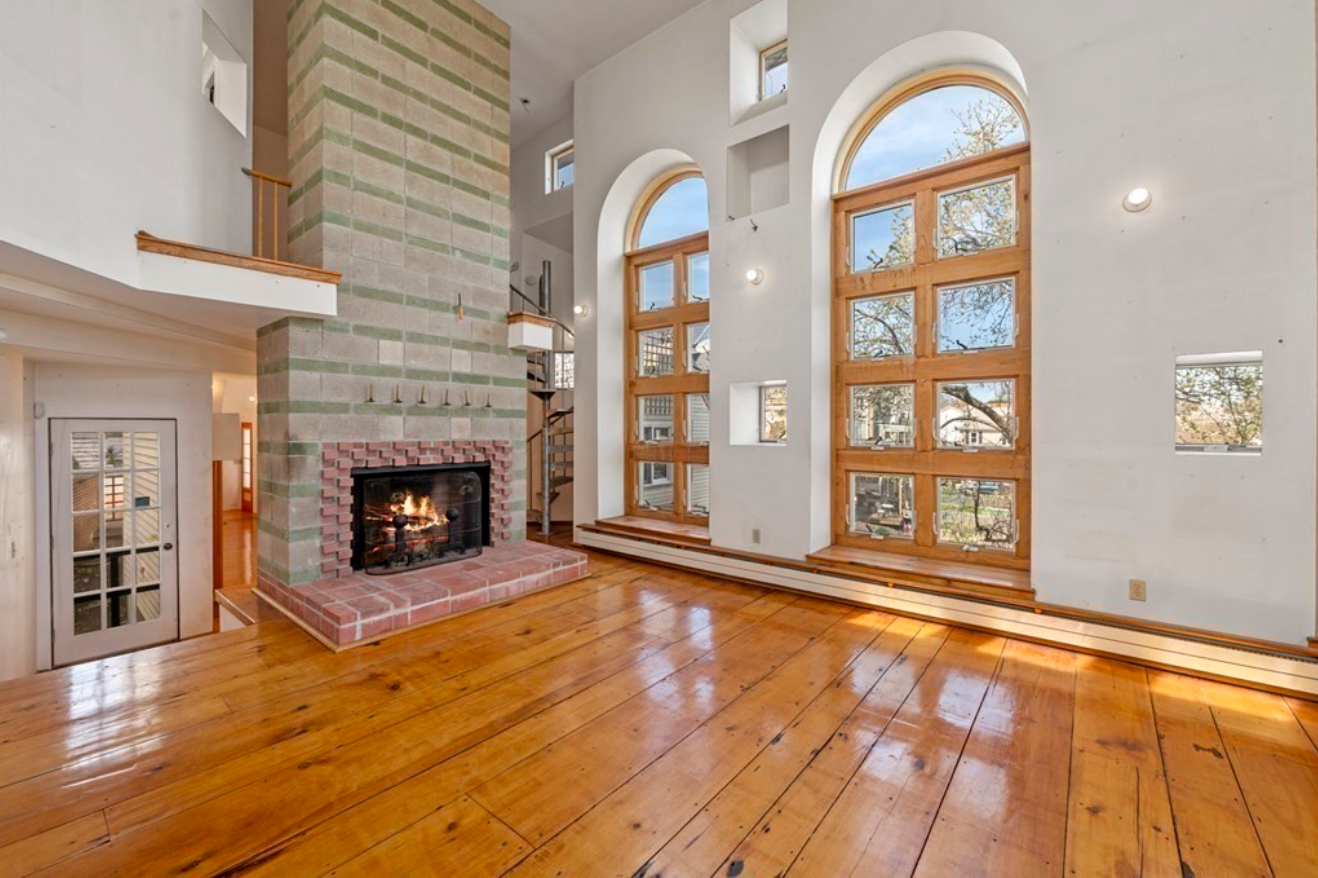 Great room with picture windows, hardwood floors, and fireplace lined in colorful brick.