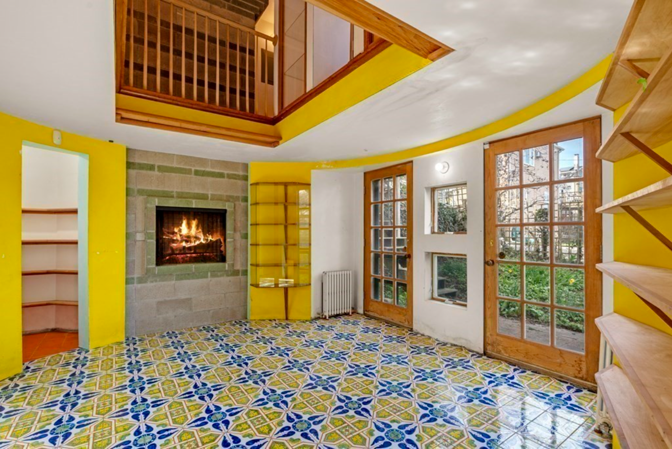 The Florida room in this Gloucester home has rounded yellow walls and built-in shelving, and is tiled with blue and yellow ceramic floor tiles.