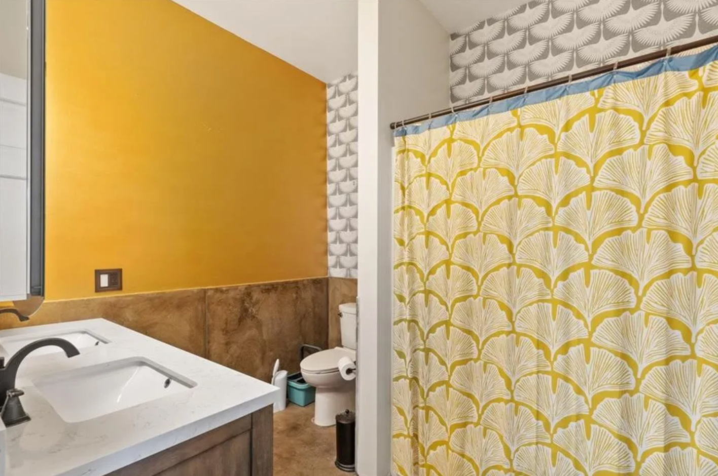 Full bathroom with combination shower-bathtub and yellow walls with grey and white accent wallpaper.