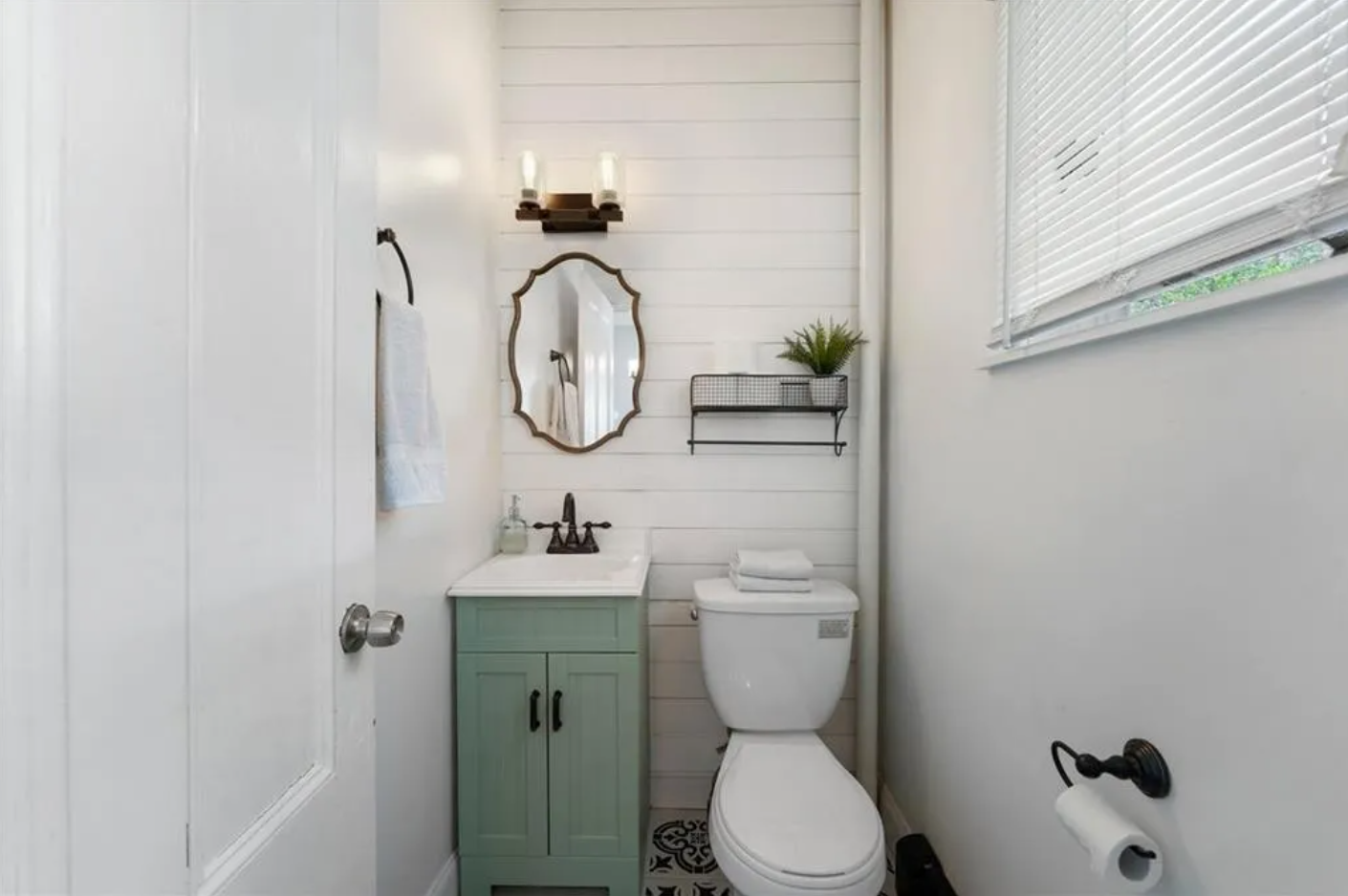 Bathroom with white walls and single vanity with sage green cabinetry.