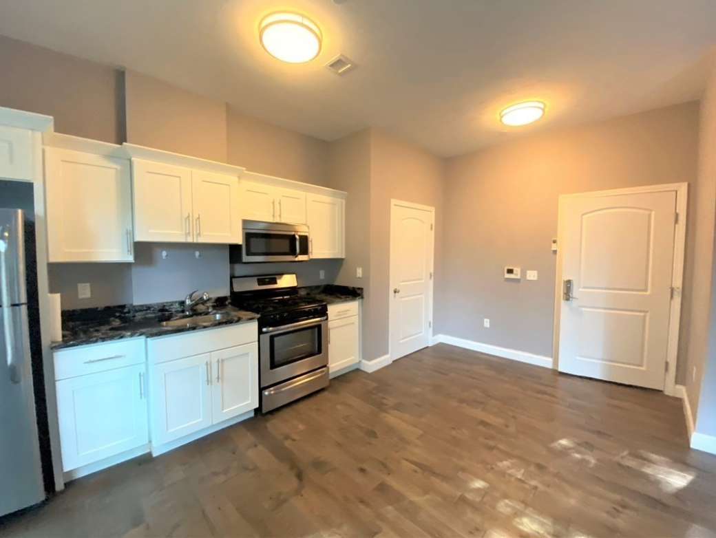 Kitchen with white Shaker-style cabinets, stainless steel appliances, and hardwood floors.
