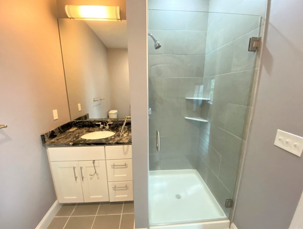 Bathroom with walk-in shower, single vanity, and grey tiled flooring.