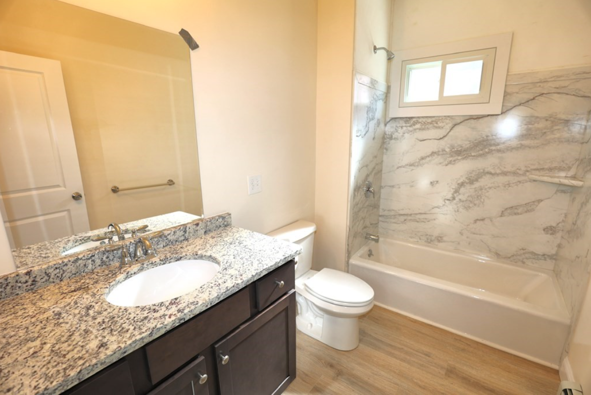 Bathroom with single vanity and combination shower-bathtub, hardwood floors, and single-hung window in the shower.