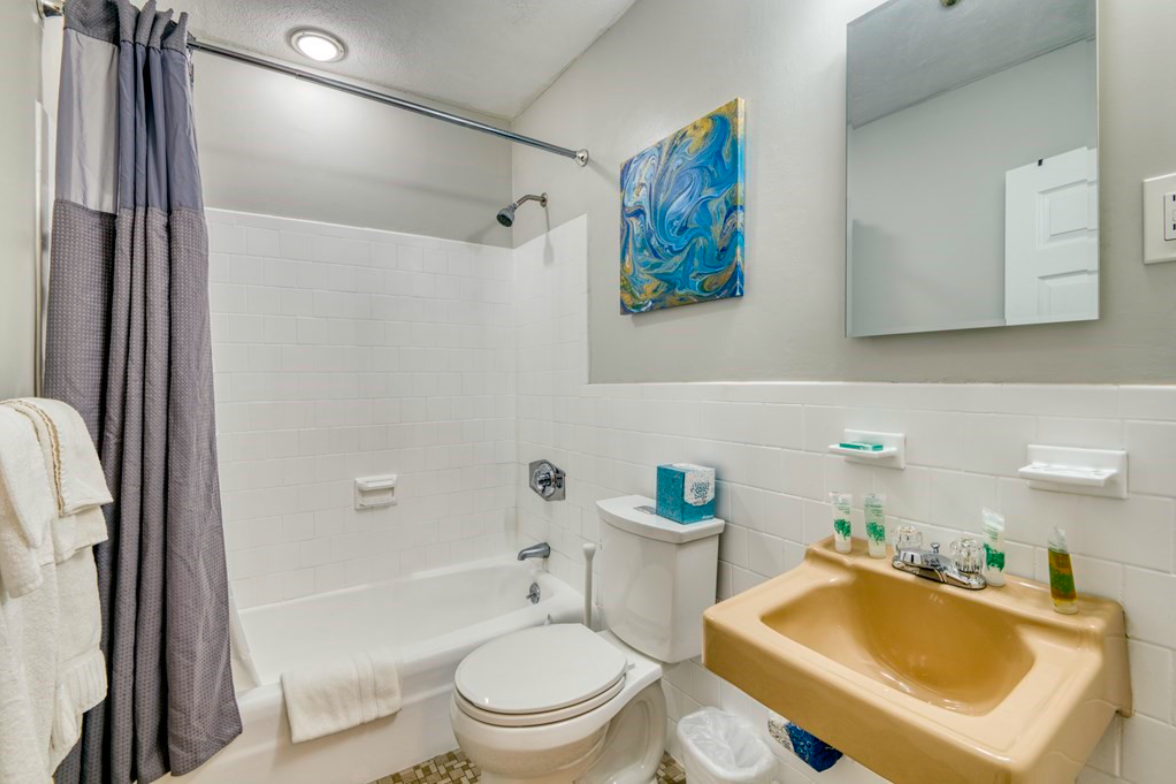 Bathroom with single combination shower-bathtub and single vanity with sunshine yellow sink.
