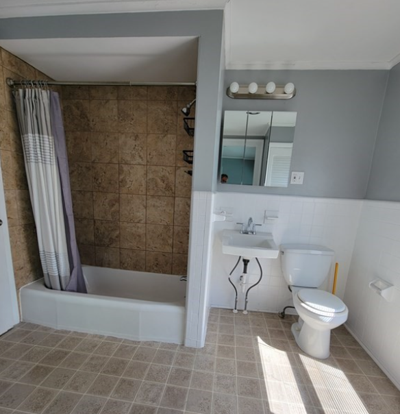 Bathroom with single vanity and combination shower-bathtub, grey walls, and beige tiled floors.