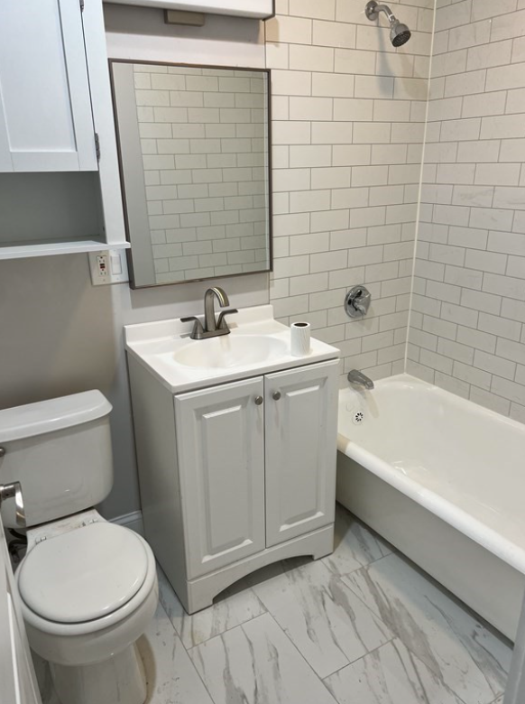Bathroom with combination shower-bathtub with white subway tiling and single vanity with white cabinetry.