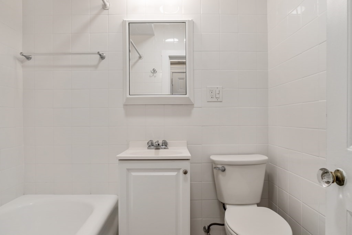 Bathroom with single vanity, combination shower-bathtub, and white tiling.