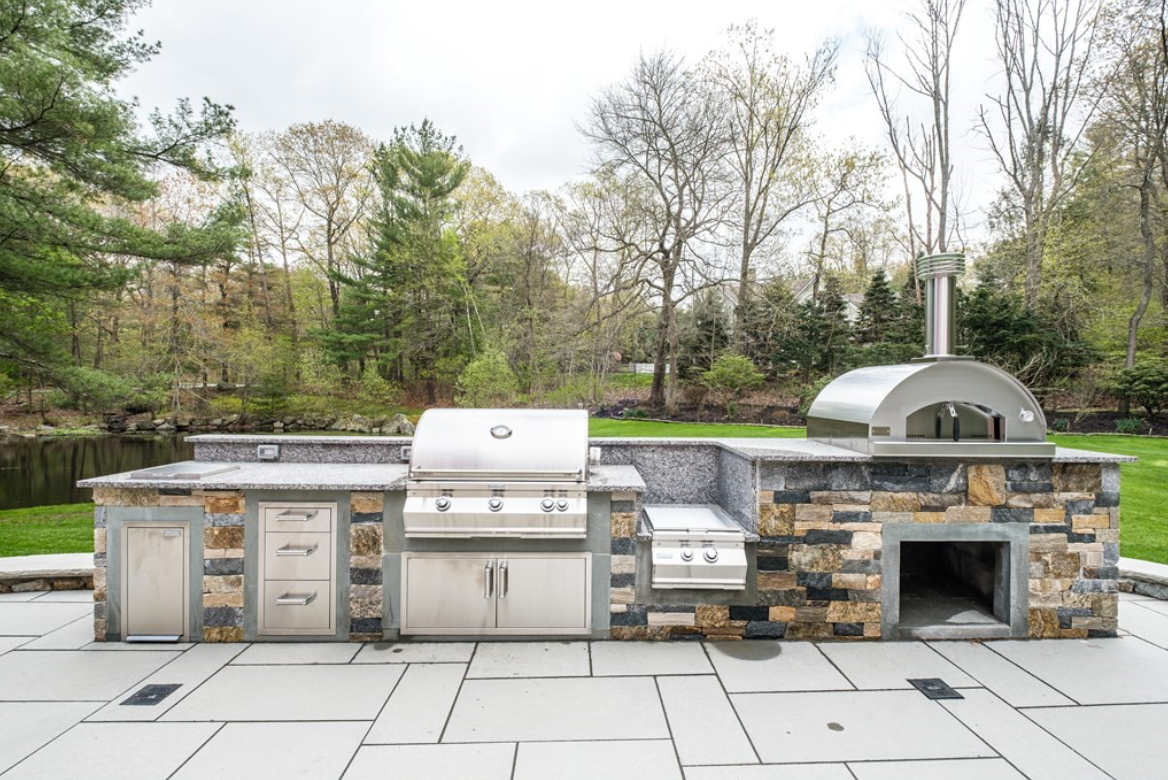 Outdoor kitchen with grill, brick oven, and built-in storage.