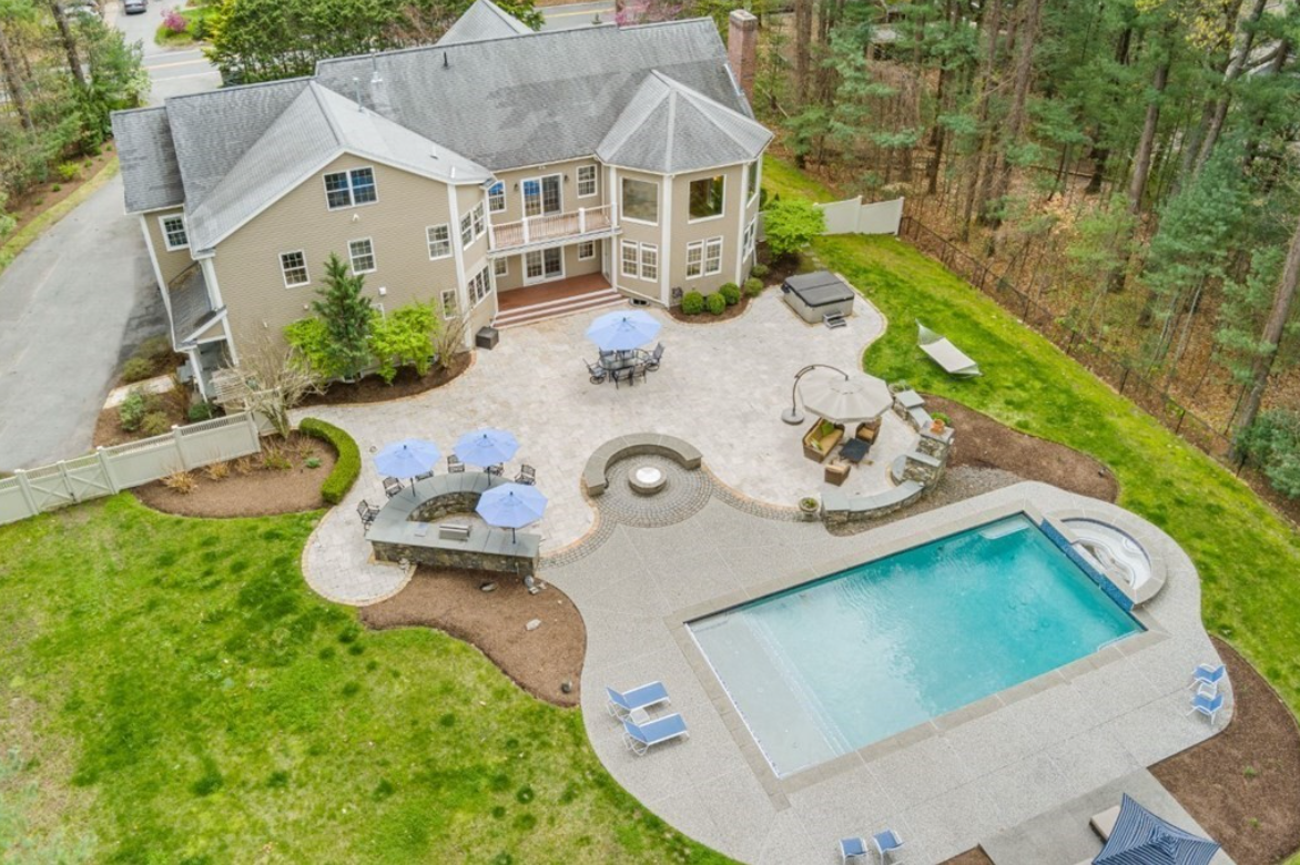 Aerial view of colonial home with brick patio and outdoor, in-ground pool.