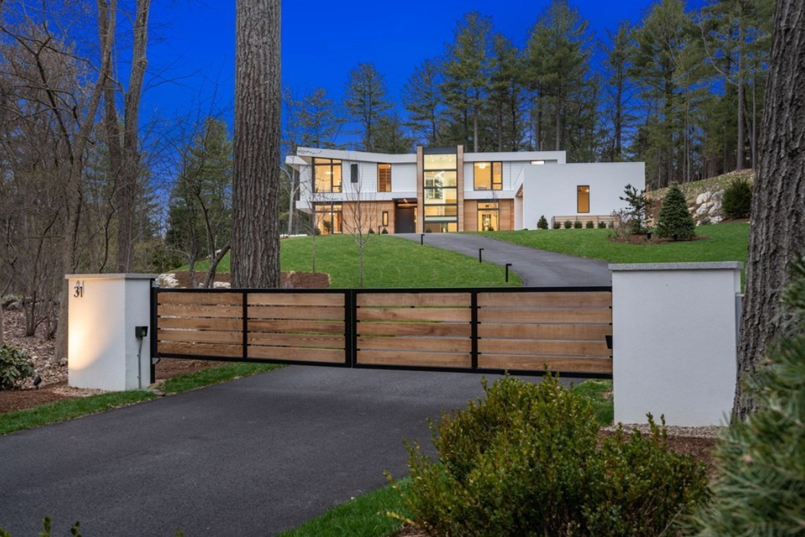 Contemporary home illuminated at night behind wooden gate.