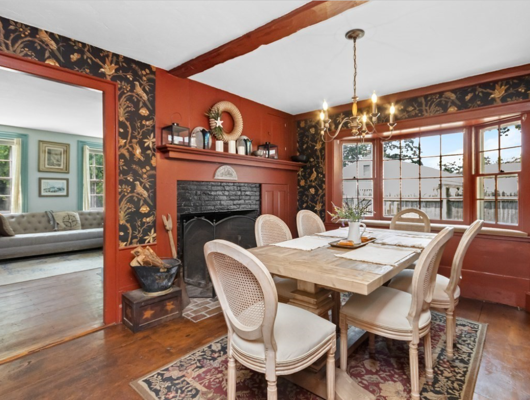 Dining room with fireplace and hardwood floors. The walls are painted a rusty red and accented with floral wallpaper.