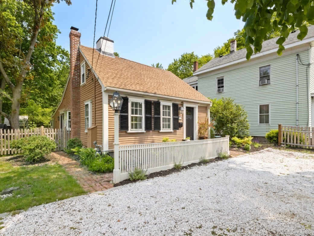 Light brown cape with dark shutters and brick chimney.