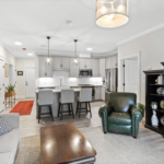 Living room with light gray walls, drum chandelier, and open floor plan leading to kitchen. A home in Lakeville is used to illustrate homes for sale in Massachusetts.