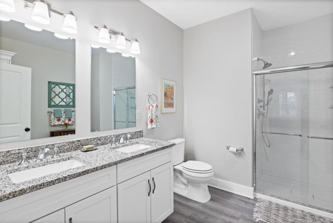 Bathroom with double vanity, walk-in shower, light gray walls and gray floors.