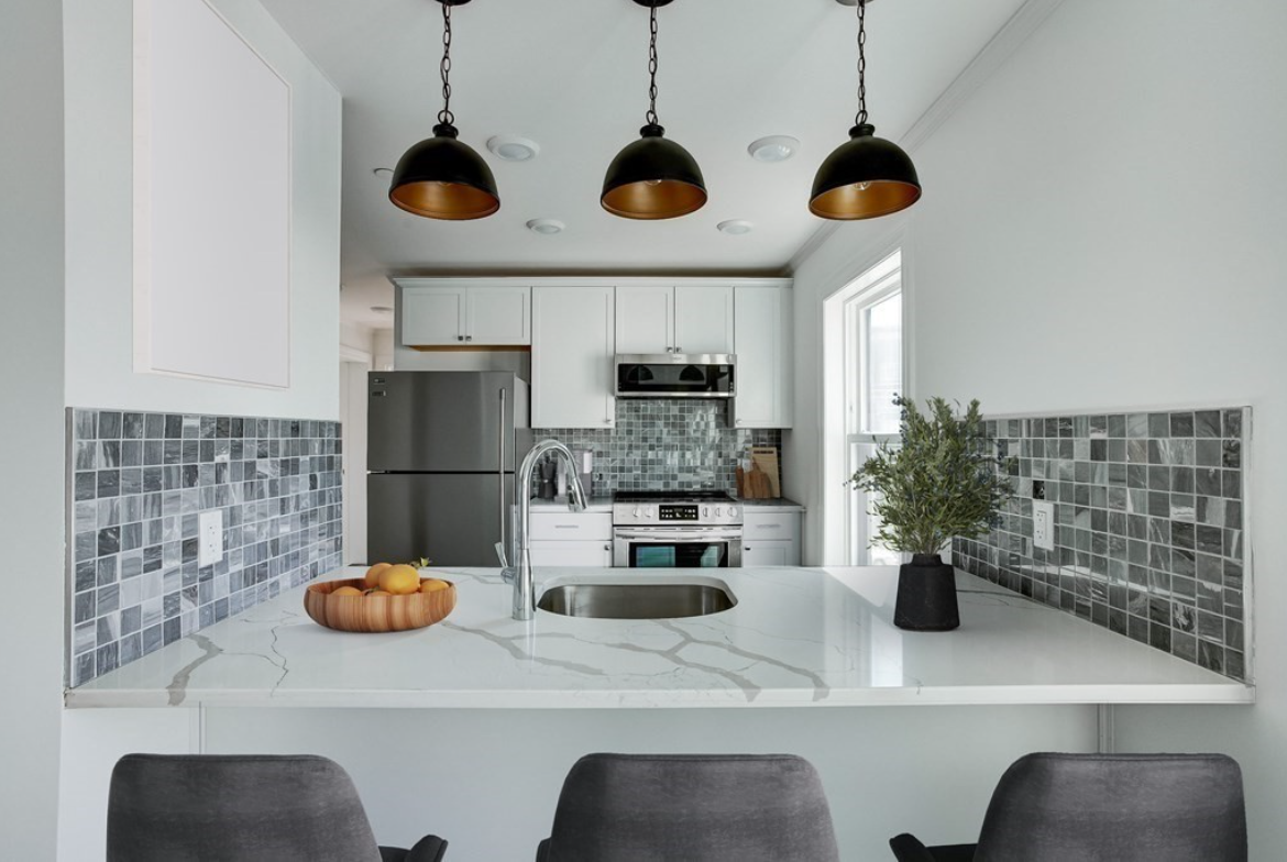 Kitchen with pendant lighting, gray backsplash, server's window, and white cabinetry.
