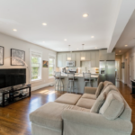 Kitchen and living room with beige walls, overhead lighting, and single-hung windows.