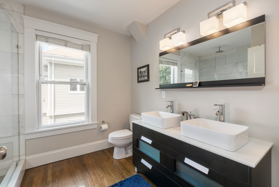 Bathroom with double vanity and single-hung window. The vanity has black cabinetry and geometric sconce lighting.