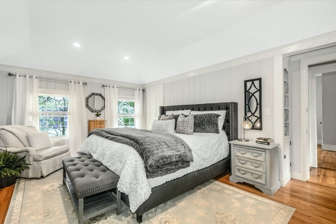 Bedroom with hardwood floors, light gray bead board walls, scallop trim, and single-hung windows with muntins.