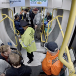An MBTA Transit Police officer, wearing a fluorescent yellow jacket and black cap, can be seen assessing the damaged floor and clearing the area inside a Green Line train as several passengers look on.