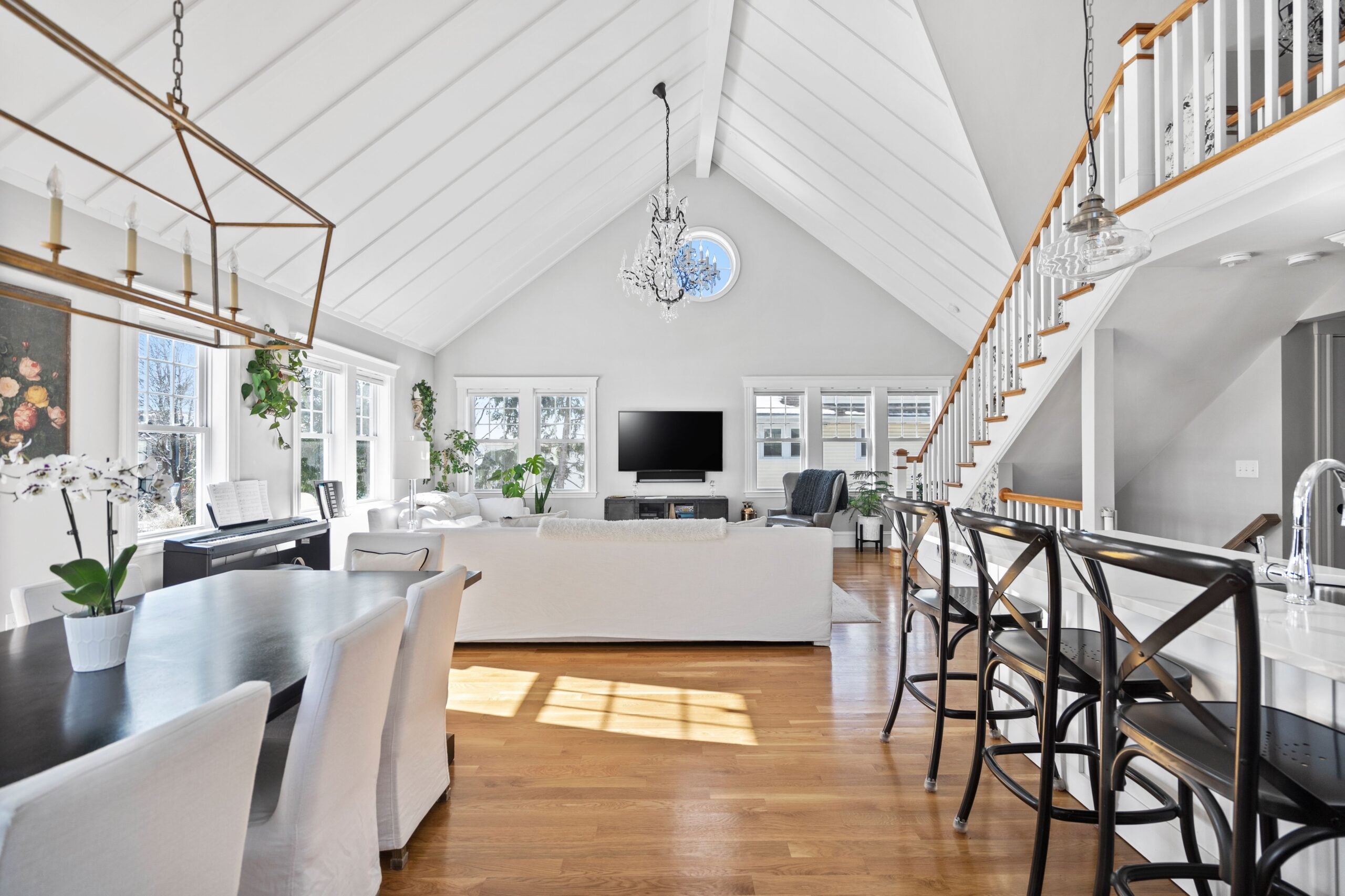 A long view from the dining area and kitchen island out toward the living area in the back. The walls are light-colored. The ceiling is white and clad in shiplap. An iron chandelier hangs from the ceiling of this Newton condo, our Home of the Week.