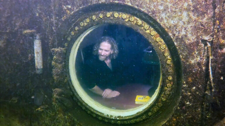 Diving explorer and medical researcher Dr. Joseph Dituri peers out of a large porthole, Saturday, May 13, 2023, at Jules' Undersea Lodge positioned at the bottom of a 30-foot-deep lagoon in Key Largo, Fla.