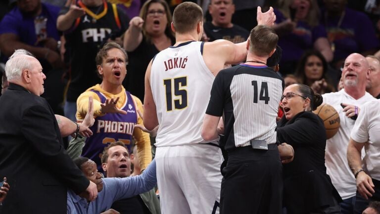 Nikola Jokic reached for the basketball after pushing off Suns owner Mat Ishbia (seated, third from left) during the first half of Game 4 Sunday.
