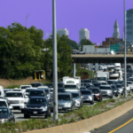 Cars sit in traffic on Route 93 north. The Boston skyline is visible in the background and the sky is tinted purple.