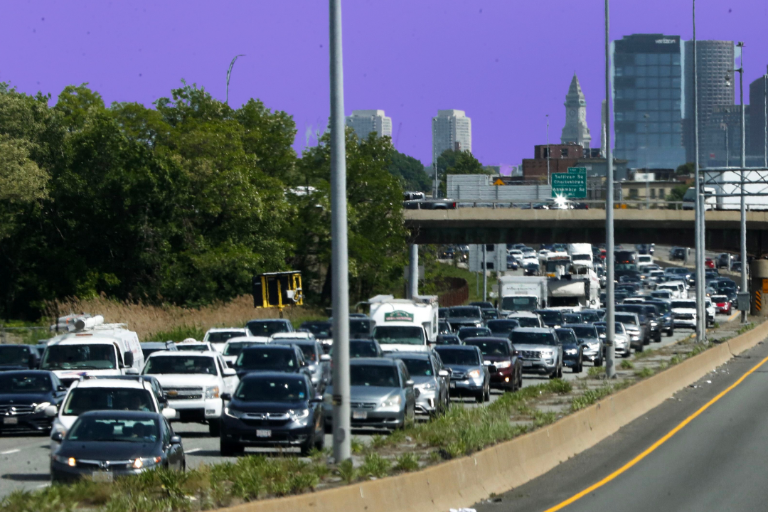 Cars sit in traffic on Route 93 north. The Boston skyline is visible in the background and the sky is tinted purple.