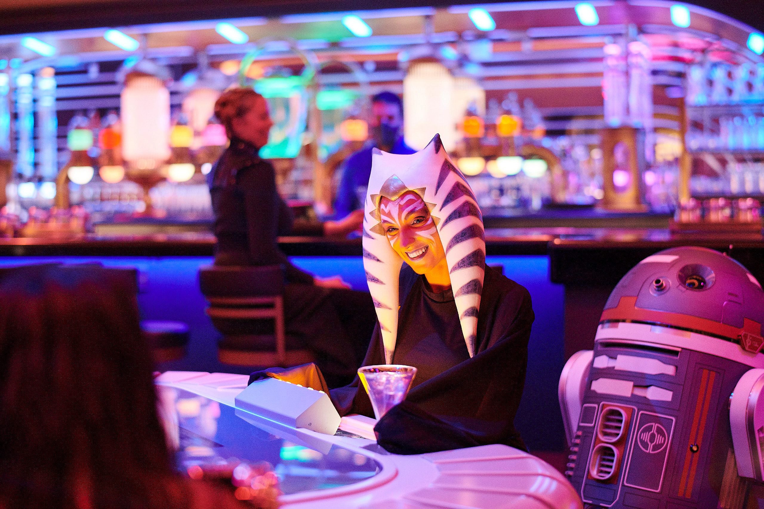 A passenger wearing a Togruta headpiece sits at the holo-sabacc table in the Star Wars: Galactic Starcruiser.