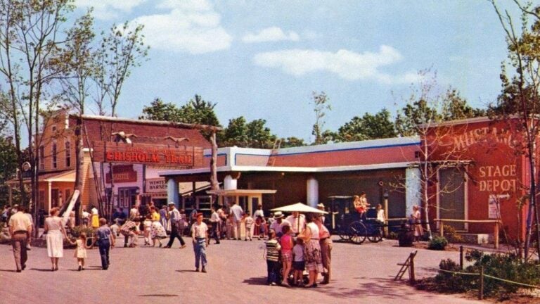 A vintage photo from the mid-20th century showing the Pleasure Island theme park. Families can be shown milling around an area with Old West-themed storefronts.