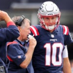 Patriots quarterback Mac Jones (right) listens to head coach Bill Belichick (left) on the sidelines. Joe Judge is at far left. The New England Patriots hosted the Baltimore Ravens in a regular season NFL football game at Gillette Stadium.