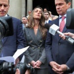Karen Read, center, is shown wearing a dark gray suit and standing outside the courthouse, flanked by two of her attorneys.