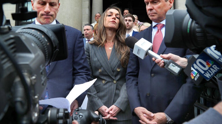 Karen Read, center, is shown wearing a dark gray suit and standing outside the courthouse, flanked by two of her attorneys.