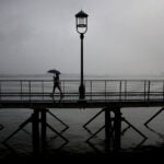 Boston weather , MA - 7/1/2020: A woman uses an umbrella to protect herself from the rain on the Harborwalk in the Seaport District of Boston