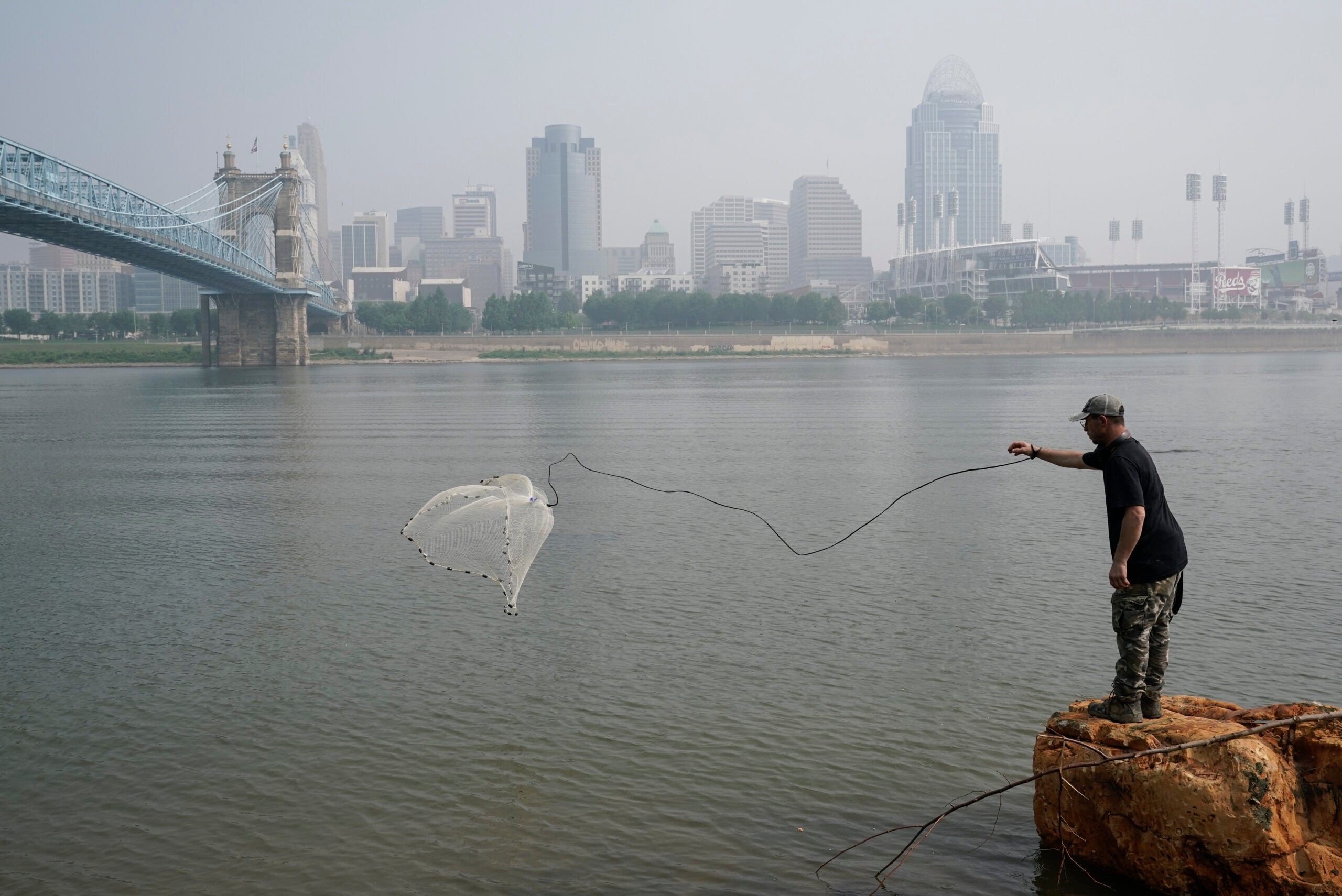 A man tosses a fishing net into the Ohio River.
