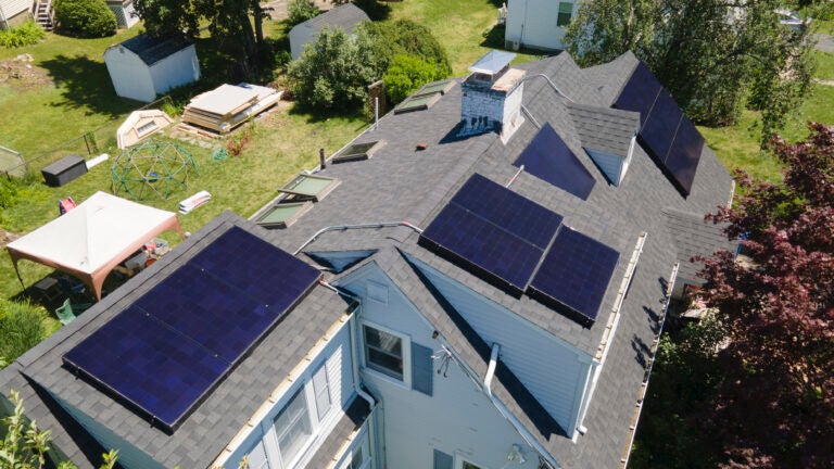 Solar panels line the roof of a modified Cape broken up by a chimney and dormers.