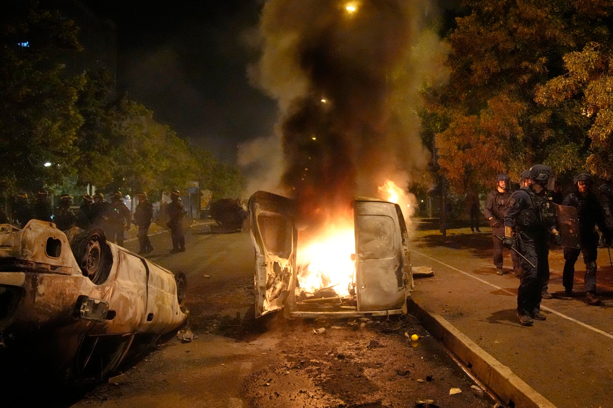 Police forces walk past burning cars in Nanterre.