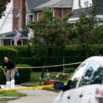 An investigator ducks under police tape as he leaves the home on Broadway Street in Newton on Sunday.