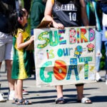 Vicky Chiong, 6, holds a Sue Bird sign with Olivia Chiong as they wait to enter Climate Pledge Arena .