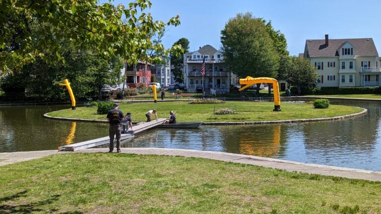 Three yellow inflatable tube men overlook a pond