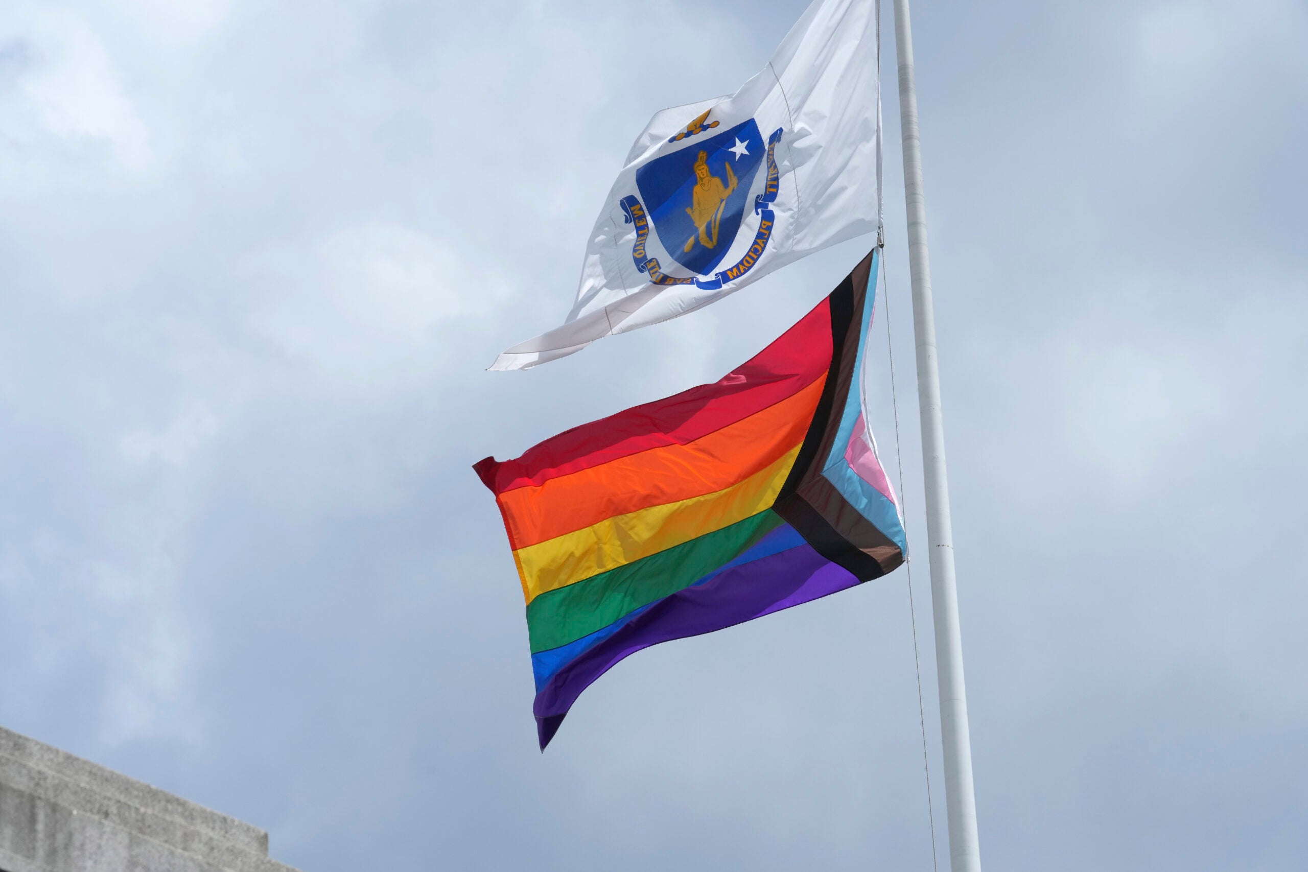 A Pride flag flies below a Massachusetts state flag in front of the Statehouse following a Pride Month Celebration.