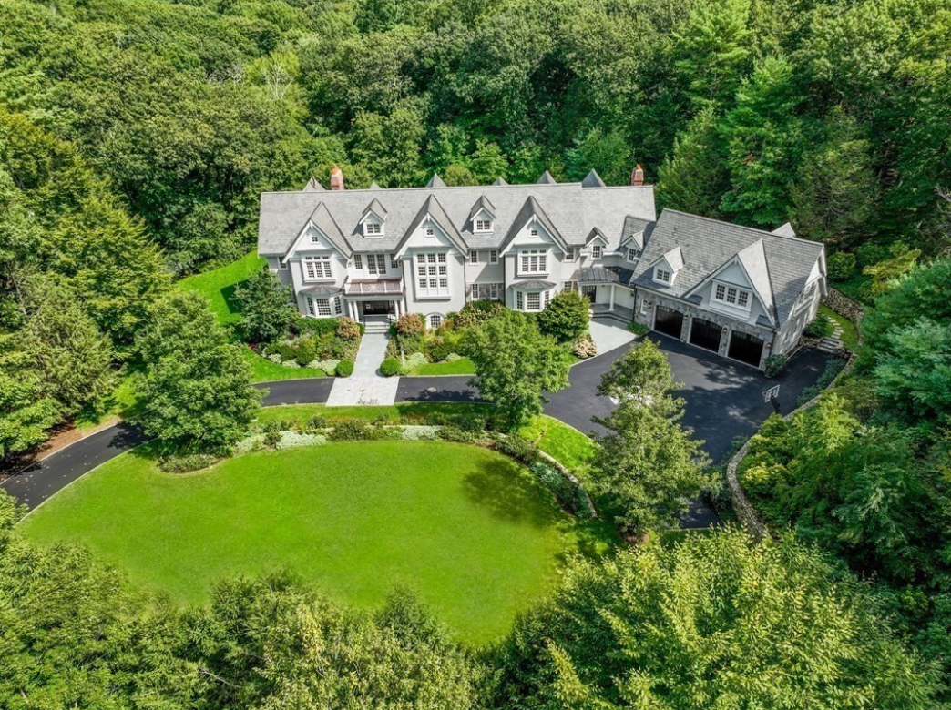 Aerial view of a stone and shingled estate with attached three-car garage.