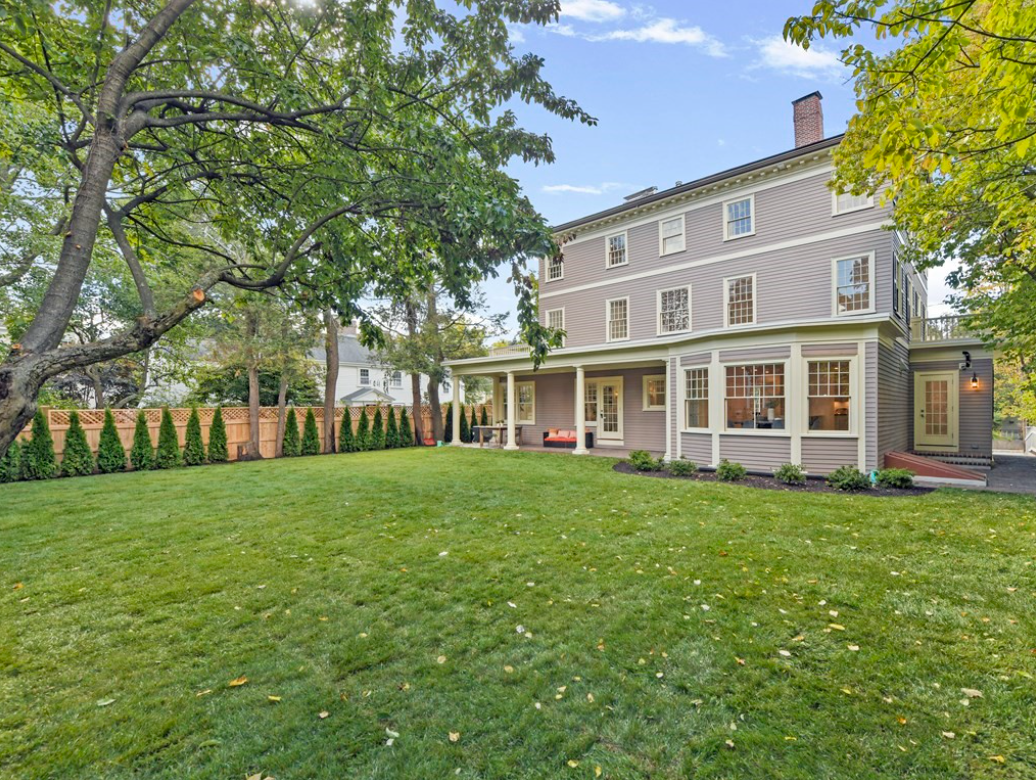 Backyard of colonial with white trim and covered porch.
