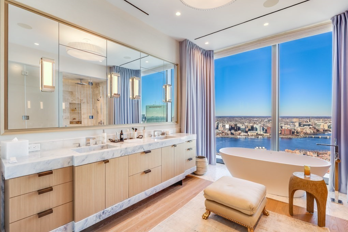 Bathroom with double vanity and soaking tub. Floor-to-ceiling windows look onto the Boston skyline and Charles River.