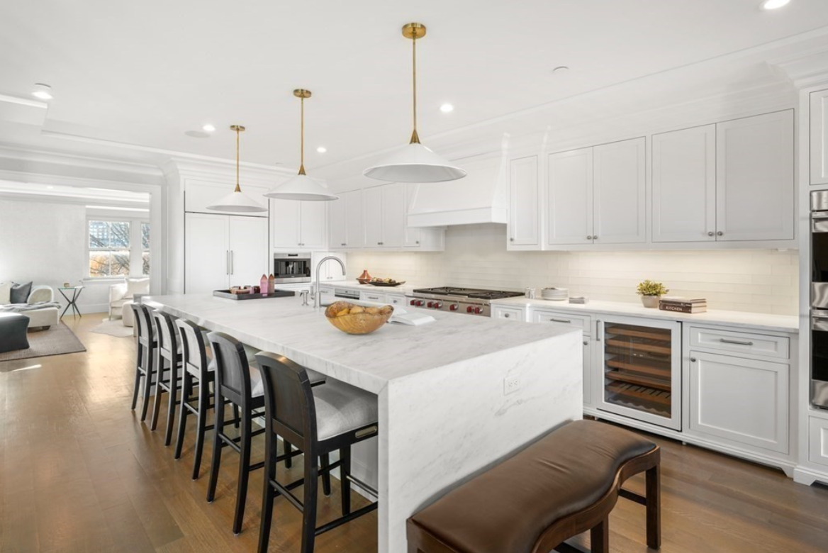 Kitchen with white Shaker-style cabinets, stainless steel appliances, wine fridge, and a waterfall island with seating for five.