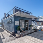 Slate blue houseboat with front porch and upper deck.