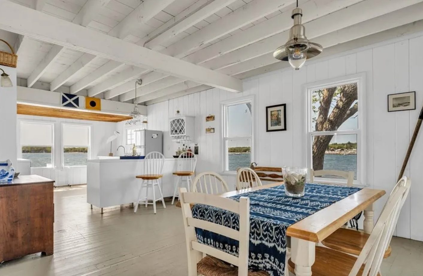 Kitchen and dining area with shiplap walls, white wooden ceiling beams, and single-hung windows.