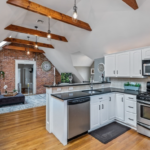 Living area with hardwood floors, cathedral ceilings and exposed wood ceiling beams, and exposed brick accent wall.