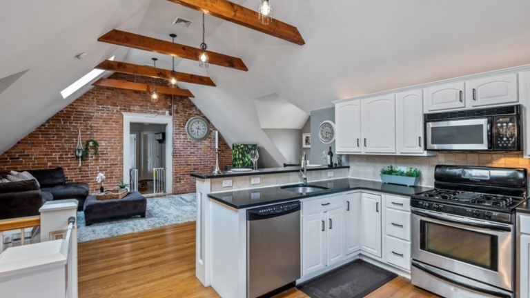 Living area with hardwood floors, cathedral ceilings and exposed wood ceiling beams, and exposed brick accent wall.