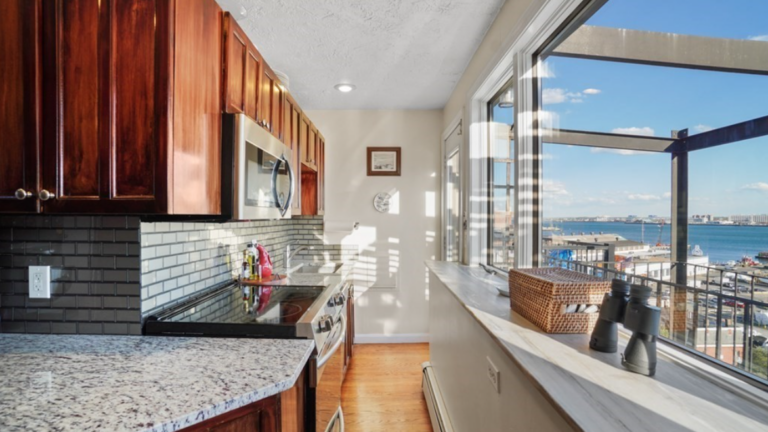 Kitchen with hardwood floors and Shaker-style cabinets. The kitchen is across a hallway from picture windows overlooking Boston Harbor.